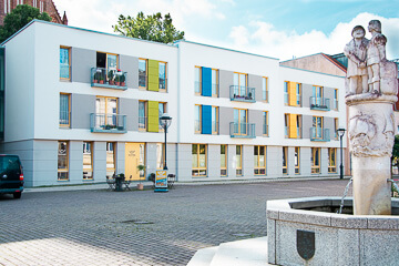 Das Gebäude des Betreuten Wohnens in Demmin auf dem Marktplatz hinter einem Brunnen