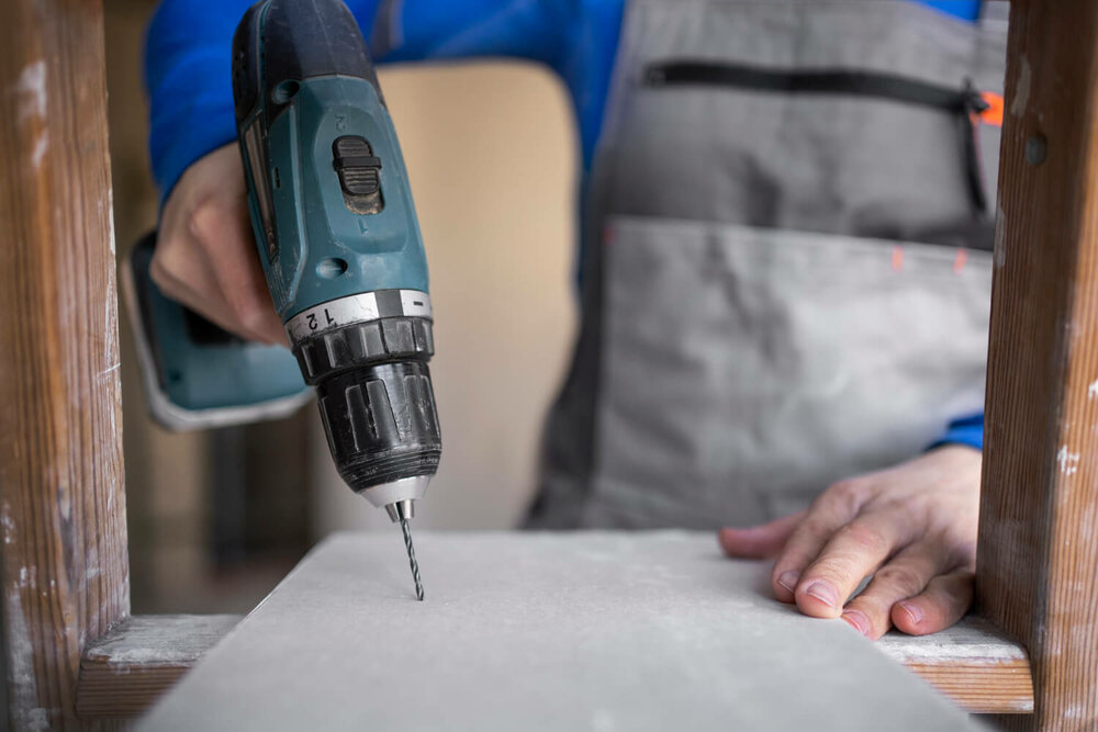 Ein Mann in Arbeitskleidung bohrt mit einem Bohrer in eine Platte 